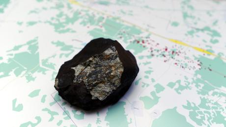 Das 508 Gramm schwere Stück eines Meteoriten stürzte am 15. Februar bei Tscheljabinsk ab. Dunkel ist die Schmelzkruste, das helle Teil ist das „Fenster“. Im Hintergrund eine Karte, auf der Karl Wimmer die Flugkurve der Steine erfasst hat. Im Fallen wurde der Stein vom Wind abgelenkt, deswegen machte er scheinbar einen Haken. 
