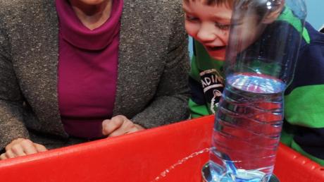 Sozialministerin Emilia Müller verfolgt im Kindergarten St. Oswald in Leitershofen mit Moritz ein Experiment mit einer Wasserflasche. 
