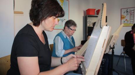 Ulrike Schollerer konzentriert sich auf das Harfenspiel bei einem Probetermin, hinter ihr sitzt Helga Reitschuster. Das eingeschobene Notenblatt erleichtert das Musikzieren. 