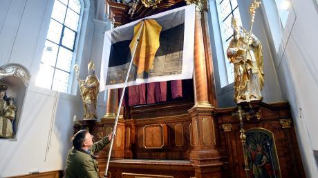 Der Mesner der Gablinger Kirche St. Martin, Helmut Scharpf, balanciert das Miserortuch mit dem Titel „Gott und Gold – Wie viel ist genug?“ mit viel Geschick vor das Altarbild. 