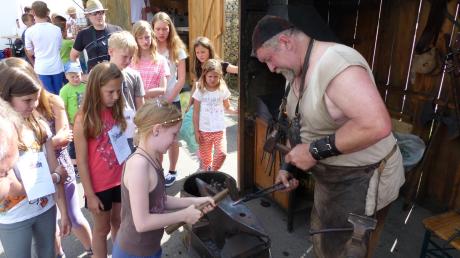 Die neunjährige Marietta aus Wertingen konzentriert sich, um genau auf das kleine Stückchen heißes Eisen zu treffen, das später ihr hufeisenförmiger Anhänger werden soll. 	