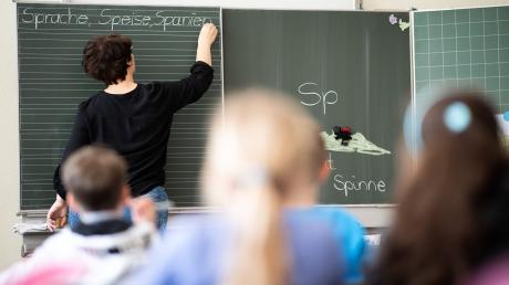 Eine Lehrerin schreibt in einer Schule an die Tafel. Der anhaltende Personalmangel und die Corona-Pandemie verstärken die körperliche und mentale Erschöpfung der Lehrkräfte.