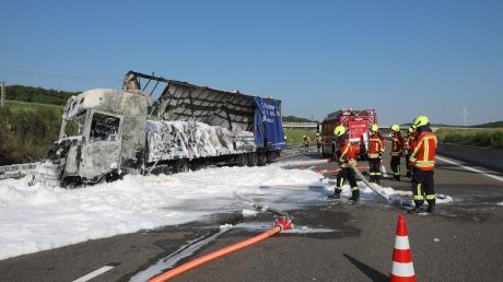Einsatzkräfte der Feuerwehr richten einen Schlauch auf einen ausgebrannten Lastwagen.