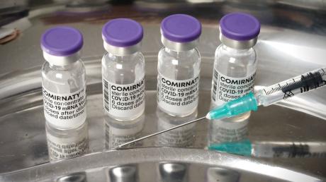 Eine Spritze liegt in einer Arztpraxis neben Ampullen des Corona-Impfstoffes von Biontech/Pfizer.
