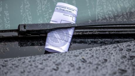 Ein Knöllchen steckt bei Regen unter dem Scheibenwischer eines Autos, das falsch geparkt wurde.