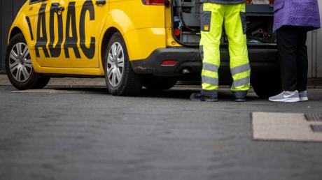 Ein Mitarbeiter des ADAC steht mit seinem gelben Fahrzeug an einer Straße und hilft einer Frau.