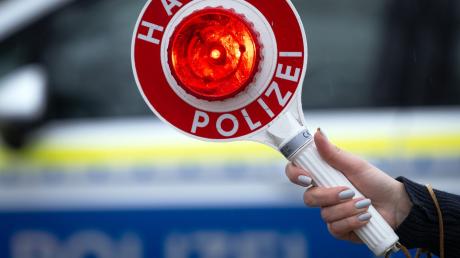 Eine Polizistin hält während einer Verkehrskontrolle eine Polizeikelle mit der Aufschrift "Halt Polizei".