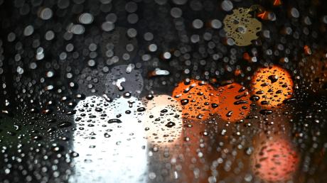 Lichter von Fahrzeugen scheinen durch eine Autoscheibe, die mit Regentropfen bedeckt ist.