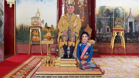 König Maha Vajiralongkorn im Juli 2019 auf seinem Thron in Bangkok. Zu seinen Füßen Zweitfrau Sineenat Wongvajirapakdi, die er kurz danach verstieß, nun aber wieder begnadigt hat.