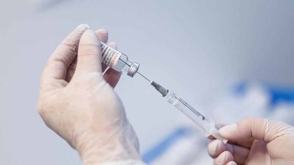 Die Mitarbeiterin eines Impfzentrums zieht den Corona-Impfstoff Nuvaxovid mit einer Spritze auf.