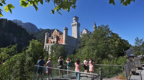 Touristen stehen auf einer Aussichtsplattform vor dem Schloss Neuschwanstein.