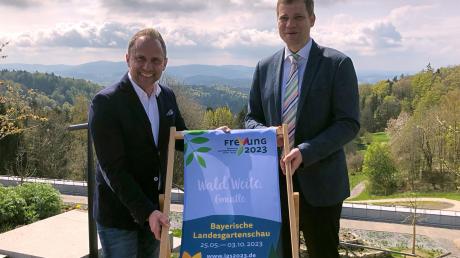 Bayerns Umweltminister Thorsten Glauber (Freie Wähler, r) und der Bürgermeister der Stadt Freyung, Olaf Heinrich (CSU), halten einen Liegestuhl mit dem Logo der Landesgartenschau 2023.
