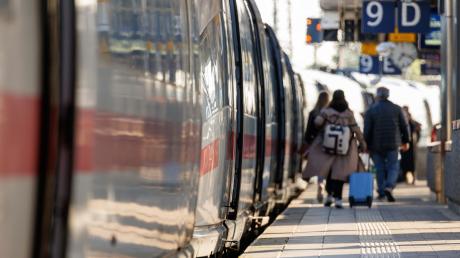 Reisende gehen mit Gepäck am Bahnsteig am Nürnberger Hauptbahnhof neben einem ICE entlang.
