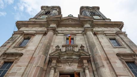 Eine vom Wind verfangene Regenbogenflagge hängt über dem Eingang der Kirche St. Egidien.