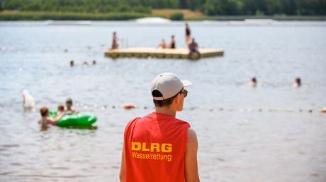 Ein Mitglied der Deutschen Lebens-Rettungs-Gesellschaft (DLRG) steht in einem Strandbad am Ufer.