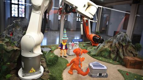 Kasperle und Drache Famulus werden in einer Glasvitrine von Kuka-Robotern gesteuert.