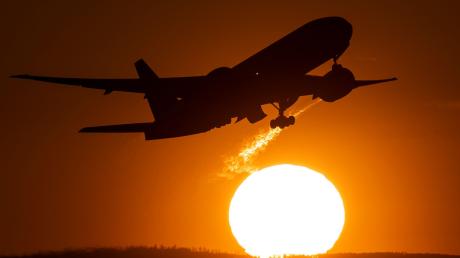 Eine Passagiermaschine hebt vor der untergehenden Sonne von einem Flughafen ab.