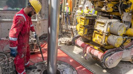 Arbeiter hantieren an einer Geothermiekraftwerk-Baustelle mit einem Bohrgestänge.