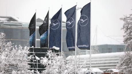 Fahnen der Lufthansa wehen am Flughafen im Schneetreiben.