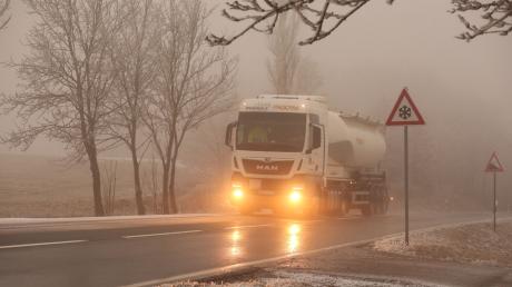 Ein Lkw fährt bei Glatteis und Nebel über eine Straße.
