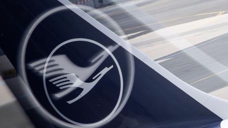 Ein Flugzeug mit dem Logo der Lufthansa auf der Heckflosse steht an einem Flughafen.