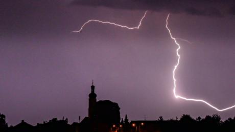 Blitze entladen sich aus einer Gewitterwolke über einer Kirche in Niederbayern.