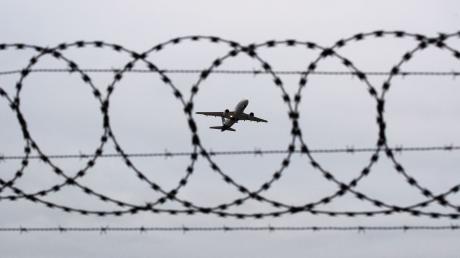 Ein Flugzeug startet - fotografiert durch Stacheldraht am Flughafenzaun.