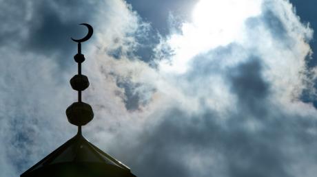 Der Halbmond auf dem Minarett einer Moschee hebt sich als Schattenriss vor Wolken ab.
