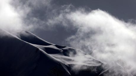 Wolken ziehen über die mit Neuschnee bedeckten Alpen.