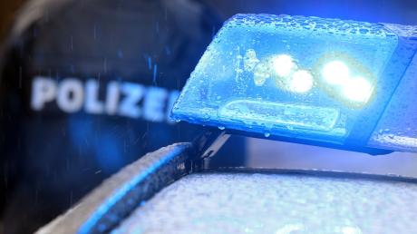 Ein Polizist steht hinter einem Streifenwagen mit eingeschaltetem Blaulicht.