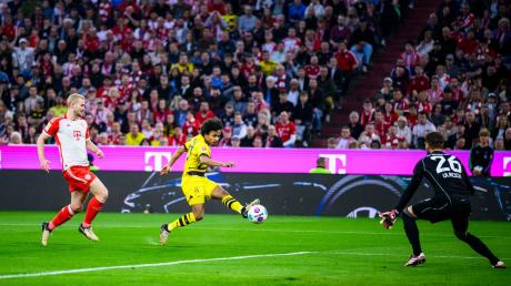 Dortmunds Karim Adeyemi (M) macht das Tor zum 0:1 gegen Münchens Matthijs de Ligt (l) und Münchens Torwart Sven Ulreich (r). (zu dpa: