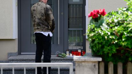 Ein Mann steht vor einem Hauseingang, auf dem Blumen und Kerzen liegen.
