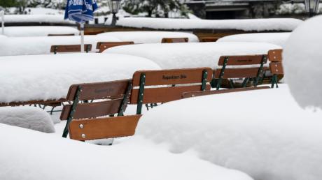 Schnee liegt auf Tischen und Stühlen in einem Biergarten am Walchensee.