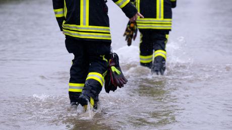 Feuerwehrleute gehen über eine überflutet Straße.