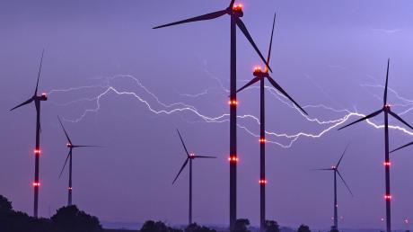 Ein Blitz erhellt den Nachthimmel über Windenergieanlagen mit roten Positionslichtern.