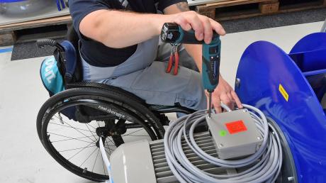 An einem Arbeitsplatz ist ein Mitarbeiter im Rollstuhl mit Montagearbeiten beschäftigt.