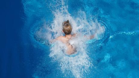 Ein Junge springt in einem Freibad ins Wasser.