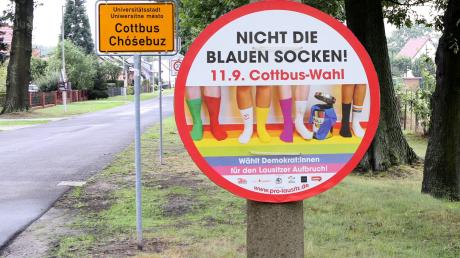 Vor dem Ortseingangsschild der Stadt Cottbus hängt an einem Pfahl ein Plakat der Kampagne «Blaue Socken».