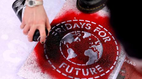 Eine Klimaaktivistin sprüht während einer Kundgebung ein Logo der Bewegung Fridays For Future auf ein Transparent.