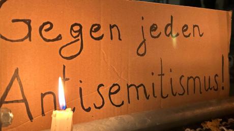 Eine brennende Kerze steht vor einem Schild mit der Aufschrift "Gegen jeden Antisemitismus".