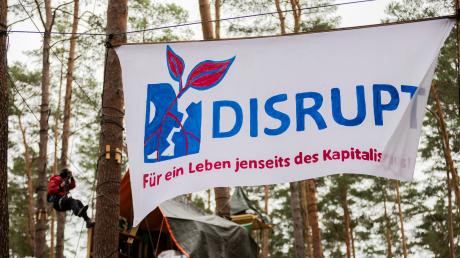 Ein Banner mit der Aufschrift  «Disrupt - für ein Leben jenseits des Kapitalismus» hängt im Camp der Initiative «Tesla stoppen» in einem Kiefernwald nahe der Tesla-Gigafactory Berlin-Brandenburg zwischen Bäumen.