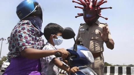 Ein Polizeibeamter im indischen Chennai trägt einen Helm, der einem Virus ähnelt, und weist Pendler auf die Einhaltung der Ausgangsbeschränkungen hin.