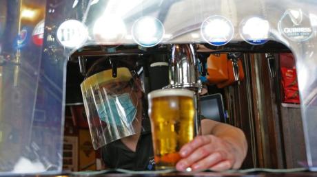 Ein Barkeeper zapft in London mit Mundschutz und Visier ein Glas Bier. 