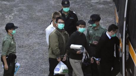 Eskortiert von Beamten des Strafvollzugs, steigen Ivan Lam (Mitte, links) und Joshua Wong (Mitte, rechts) in einen Gefangenentransporter. Die Aktivisten der Demokratiebewegung sind zusammen mit einer Mitstreiterin zu Haftstrafen verurteilt worden.