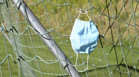 Eine Corona-Schutzmaske hat sich im Tornetz auf einem Fußballplatz verfangen.