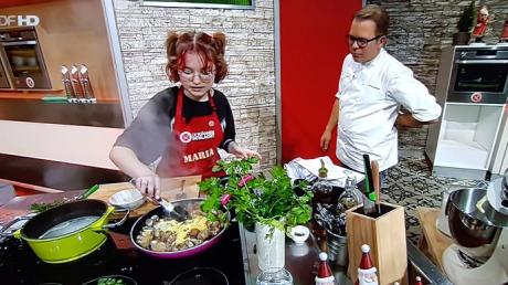 Moderator und Sternekoch Mario Kotaska schaut Maria Baumann beim Kochen zu.
