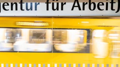 Der Schriftzug "„Agentur für Arbeit“" steht am frühen Morgen an einer Stuttgarter Haltestelle geschrieben, während im Hintergrund eine Stadtbahn einfährt.