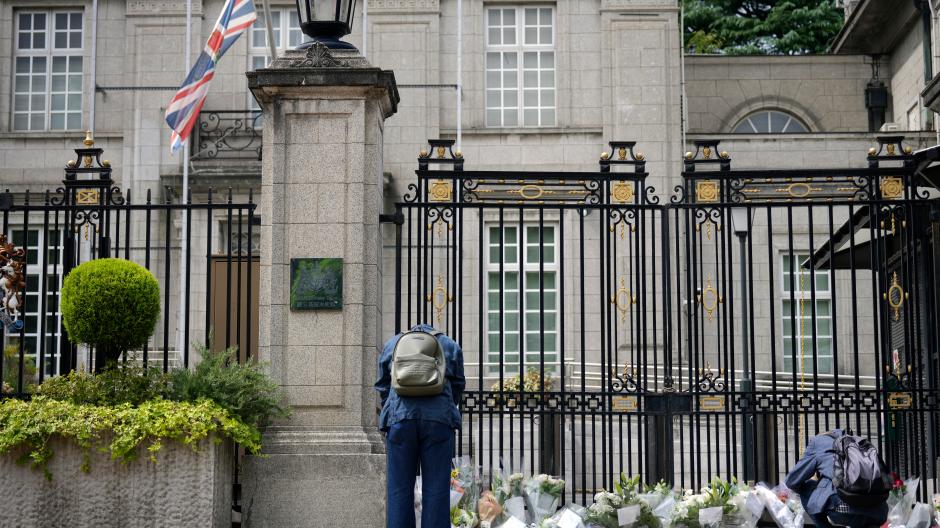Ein Mann verbeugt sich, während andere Blumen vor der britischen Botschaft niederlegen.