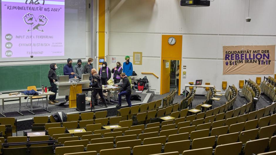 Studierende der Klimabewegung End Fossil Augsburg halten den größten Hörsaal auf dem Unicampus besetzt, der Vorlesungsbetrieb soll trotzdem weiterlaufen.