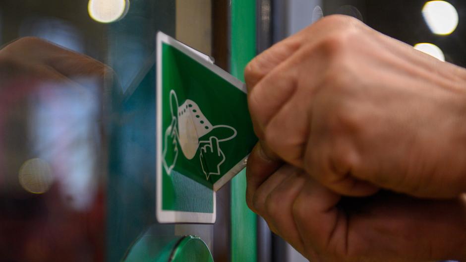 Ein Mitarbeiter der Magdeburger Verkehrsbetriebe entfernt einen Aufkleber von der Tür einer Straßenbahn, der auf die Pflicht zum Tragen einer Maske hinweist.
